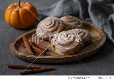 Sweet rolls with cinnamon and icing on a wooden board on a dark background with pumpkin and napkin. Sweet rolls with cinnamon and icing on a wooden board on a dark background with pumpkin and napkin. 119860494