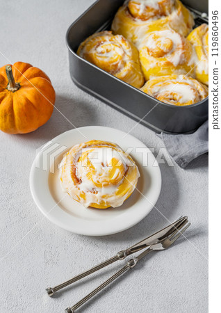 Sweet pumpkin rolls with creamy glaze and cinnamon on a plate on a light background. Sweet pumpkin rolls with creamy glaze and cinnamon on a plate on a light background. 119860496