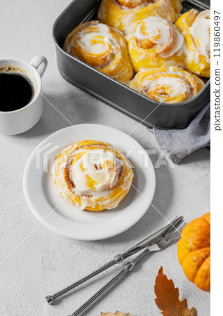 Sweet pumpkin rolls with creamy glaze and cinnamon on a plate on a light background Sweet pumpkin rolls with creamy glaze and cinnamon on a plate on a light background 119860497