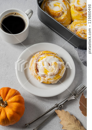 Flat lay of sweet pumpkin rolls with creamy glaze and cinnamon on a plate on a light background Flat lay of sweet pumpkin rolls with creamy glaze and cinnamon on a plate on a light background 119860498