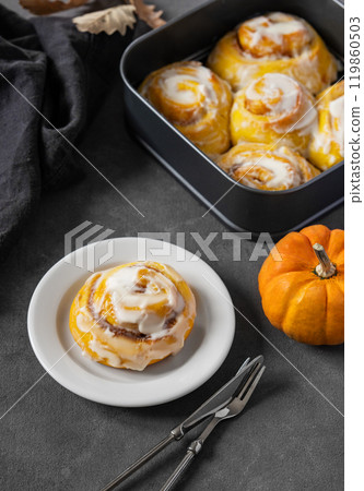 Pumpkin rolls with creamy glaze and cinnamon on a plate on a dark background. Pumpkin rolls with creamy glaze and cinnamon on a plate on a dark background. 119860503
