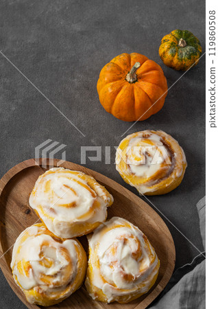 Pumpkin rolls with creamy glaze and cinnamon on a wooden plate on a dark  background. Pumpkin rolls with creamy glaze and cinnamon on a wooden plate on a dark  background. 119860508