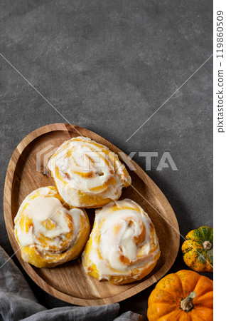 Pumpkin rolls with creamy glaze and cinnamon on a wooden plate on a dark  background. 119860509