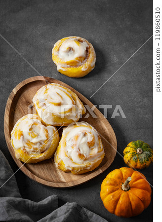 Pumpkin rolls with creamy glaze and cinnamon on a wooden plate on a dark  background. 119860510