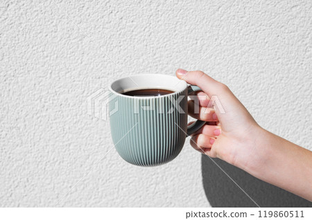 Woman hand holding green mug against textured white background in bright sunlight with shadow. 119860511