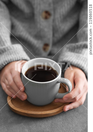 Woman in cozy sweater holding mug with espresso coffee close up on a gray table. 119860518