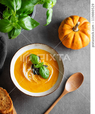 Pumpkin soup with cream, basil and seeds on a dark background with fresh pumpkins, fried bread 119860529