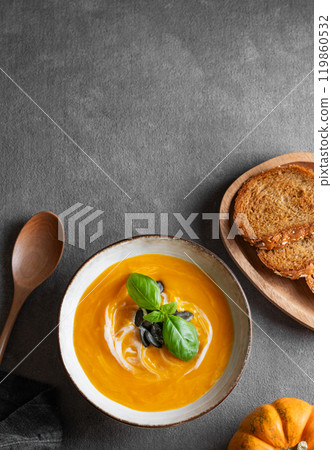 Homemade pumpkin soup with cream, basil and seeds on a dark background with  fried bread and spoon. 119860532