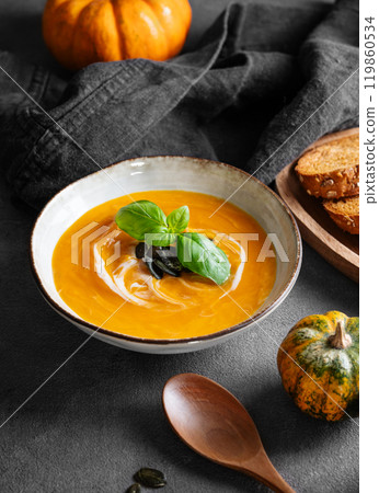Pumpkin soup with cream, basil and seeds on a dark background with fresh pumpkins, fried bread Pumpkin soup with cream, basil and seeds on a dark background with fresh pumpkins, fried bread 119860534
