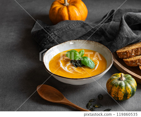 Pumpkin soup with cream, basil and seeds on a dark background with fresh pumpkins, fried bread 119860535