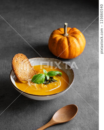 Homemade pumpkin soup with cream, basil and seeds on a dark background with bread, spoon Homemade pumpkin soup with cream, basil and seeds on a dark background with bread, spoon 119860540