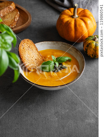 Homemade pumpkin soup with cream, basil and seeds on a dark background with bread, napkin Homemade pumpkin soup with cream, basil and seeds on a dark background with bread, napkin 119860541
