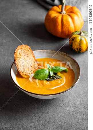 Homemade pumpkin soup with cream, basil and seeds on a dark background with bread and fresh pumpkins Homemade pumpkin soup with cream, basil and seeds on a dark background with bread and fresh pumpkins 119860542