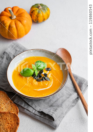 Homemade pumpkin soup with cream, basil and seeds on a light background with bread, napkin Homemade pumpkin soup with cream, basil and seeds on a light background with bread, napkin 119860543