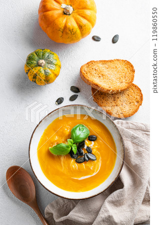 Flat lay of pumpkin soup with cream, basil and seeds on a light background with bread Flat lay of pumpkin soup with cream, basil and seeds on a light background with bread 119860550