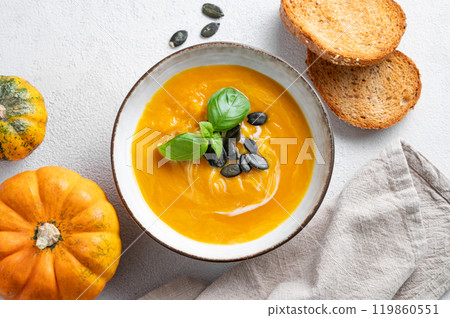 Pumpkin soup with cream, basil and seeds on a light background with bread, fresh pumpkins  119860551