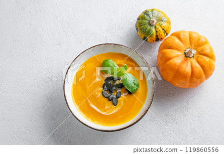 Pumpkin soup with cream, basil and seeds on a light background with fresh pumpkins. Pumpkin soup with cream, basil and seeds on a light background with fresh pumpkins. 119860556