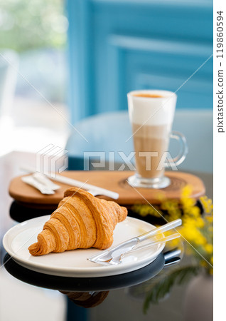 Fresh croissant on white plate and latte coffee in tall glass on table in cafe  119860594