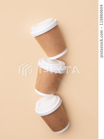 Three brown paper coffee cups with white lids on beige background. Three brown paper coffee cups with white lids on beige background. 119860604