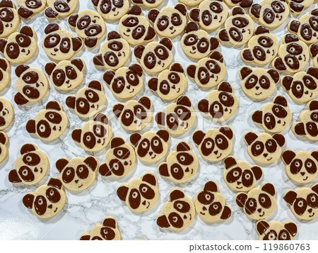 A playful assortment of panda face sugar cookies decorated with chocolate icing, forming adorable expressions. Each cookie has chocolate details for the panda eyes, nose, and ears, creating a 119860763