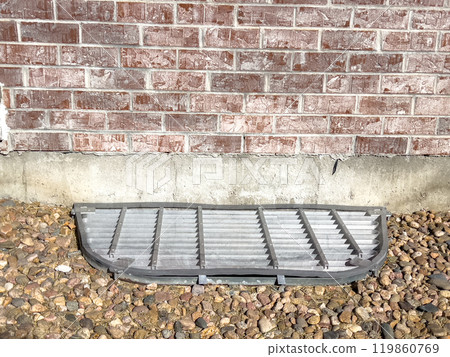A close-up view of a basement window well cover fitted with custom plexiglass on top. The cover sits securely over the window well, surrounded by decorative rocks, providing protection and allowing A close-up view of a basement window well cover fitted with custom plexiglass on top. The cover sits securely over the window well, surrounded by decorative rocks, providing protection and allowing 119860769