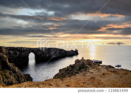 Spectacular sunset at Pont den Gil (Cala Corbetar) in Ciutadella, Menorca, Balearic Islands. Peculiar natural formation in the form of an arch Spectacular sunset at Pont den Gil (Cala Corbetar) in Ciutadella, Menorca, Balearic Islands. Peculiar natural formation in the form of an arch 119861499