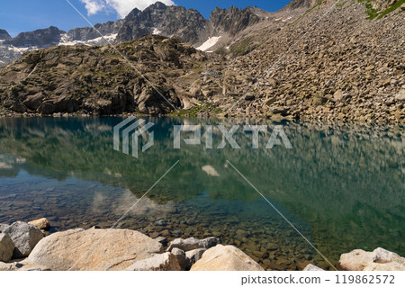 Clear mountain lake with rocky reflection and snow capped peaks in alpine landscape 119862572