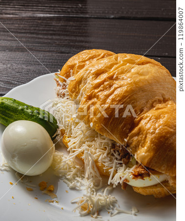 Croissant sandwich with tuna, egg, cucumber and cheese on a white plate 119864007