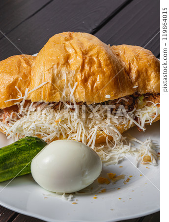 Croissant sandwich with tuna, egg and cucumber on a white plate on a dark table 119864015