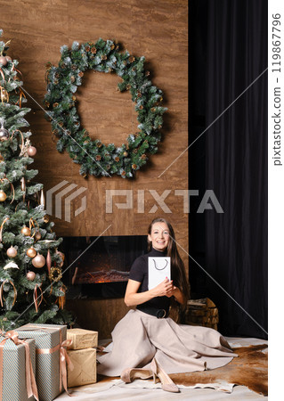 Happy woman sitting by the fireplace hugging a gift in her hands 119867796