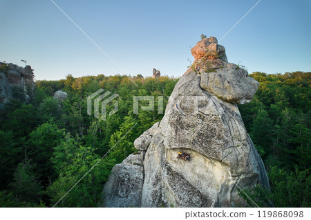 Aerial view of rock formation bathed in warm sunlight among lush green forest and rolling hills. Dovbush Rocks, Carpathian mountains, Ukraine. Aerial view of rock formation bathed in warm sunlight among lush green forest and rolling hills. Dovbush Rocks, Carpathian mountains, Ukraine. 119868098
