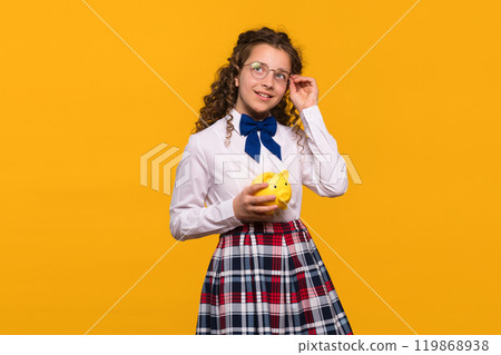 Girl adjusting glasses while holding yellow piggy bank. 119868938