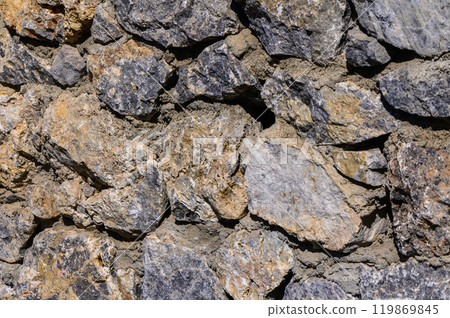 An intricate display of textured stones forming a sturdy wall in a natural outdoor setting under bright sunlight An intricate display of textured stones forming a sturdy wall in a natural outdoor setting under bright sunlight 119869845