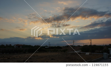 Golden rays of sunlight break through the clouds at dusk over a tranquil landscape near a quiet road Golden rays of sunlight break through the clouds at dusk over a tranquil landscape near a quiet road 119871155