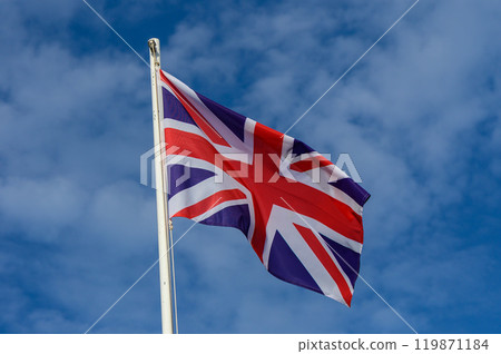 A British flag waving against a clear blue sky during a sunny day in a coastal town 119871184
