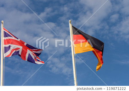 Flags of the United Kingdom and Germany waving against a vibrant blue sky on a sunny afternoon 119871222