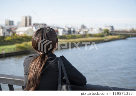 A young woman in a suit looking at the river and feeling down about her job search, career change, or work, looking up from behind, faceless A young woman in a suit looking at the river and feeling down about her job search, career change, or work, looking up from behind, faceless 119871353