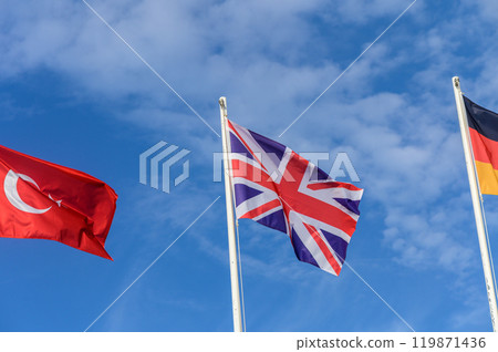 Three vibrant flags waving proudly against a bright blue sky on a sunny day, representing international unity and diversity 119871436