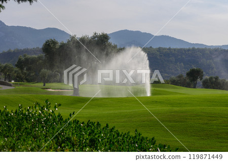 A tranquil golf course backdrop featuring a lively sprinkler amidst lush green fairways and distant mountains under a bright sky A tranquil golf course backdrop featuring a lively sprinkler amidst lush green fairways and distant mountains under a bright sky 119871449
