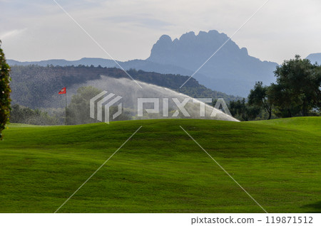 A serene afternoon at the golf course with water sprinklers dancing on the lush green fairways and mountains in the background A serene afternoon at the golf course with water sprinklers dancing on the lush green fairways and mountains in the background 119871512