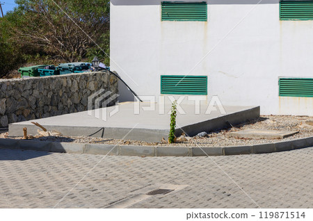 A concrete slab rests quietly at the corner of a quiet street, surrounded by nature\'s touch, hinting at upcoming construction on a sunny day 119871514