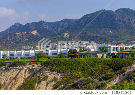 Luxurious hillside residences overlooking the vibrant coastal town beneath majestic mountains on a sunny day Luxurious hillside residences overlooking the vibrant coastal town beneath majestic mountains on a sunny day 119871561