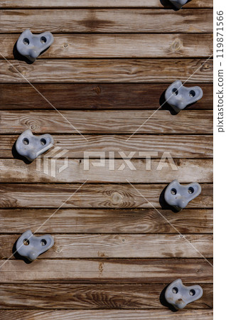 Climbing wall with textured holds against wooden backdrop on a sunny day in an outdoor fitness park 119871566