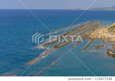 Beautiful coastal view of rocky formations extending into the turquoise sea along a sunny shoreline near an idyllic seaside town 119871586