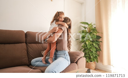 Loving mother embracing smiling girl on couch at home Loving mother embracing smiling girl on couch at home 119871713