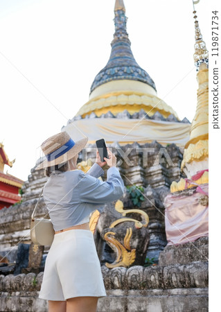 A woman is taking a picture of a building with a yellow roof A woman is taking a picture of a building with a yellow roof 119871734