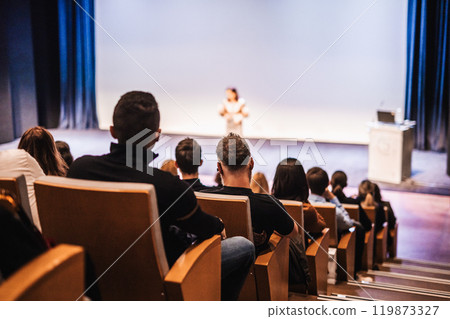 Business and entrepreneurship symposium. Female speaker giving a talk at business meeting. Audience in conference hall. Rear view of unrecognized participant in audience. Business and entrepreneurship symposium. Female speaker giving a talk at business meeting. Audience in conference hall. Rear view of unrecognized participant in audience. 119873327
