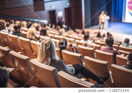 Business and entrepreneurship symposium. Female speaker giving a talk at business meeting. Audience in conference hall. Rear view of unrecognized participant in audience. Business and entrepreneurship symposium. Female speaker giving a talk at business meeting. Audience in conference hall. Rear view of unrecognized participant in audience. 119873334