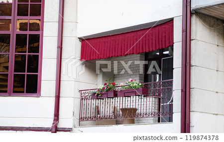 Cozy balcony with red awning and flower pots on a building facade. Cozy balcony with red awning and flower pots on a building facade. 119874378