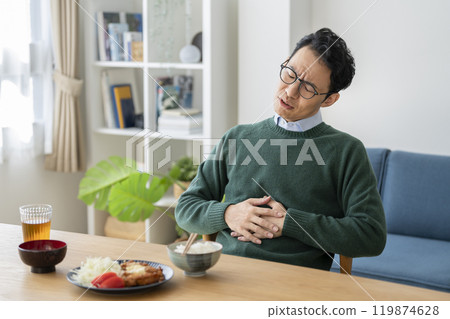 A man in his 40s holding his hand over his stomach at the dinner table 119874628